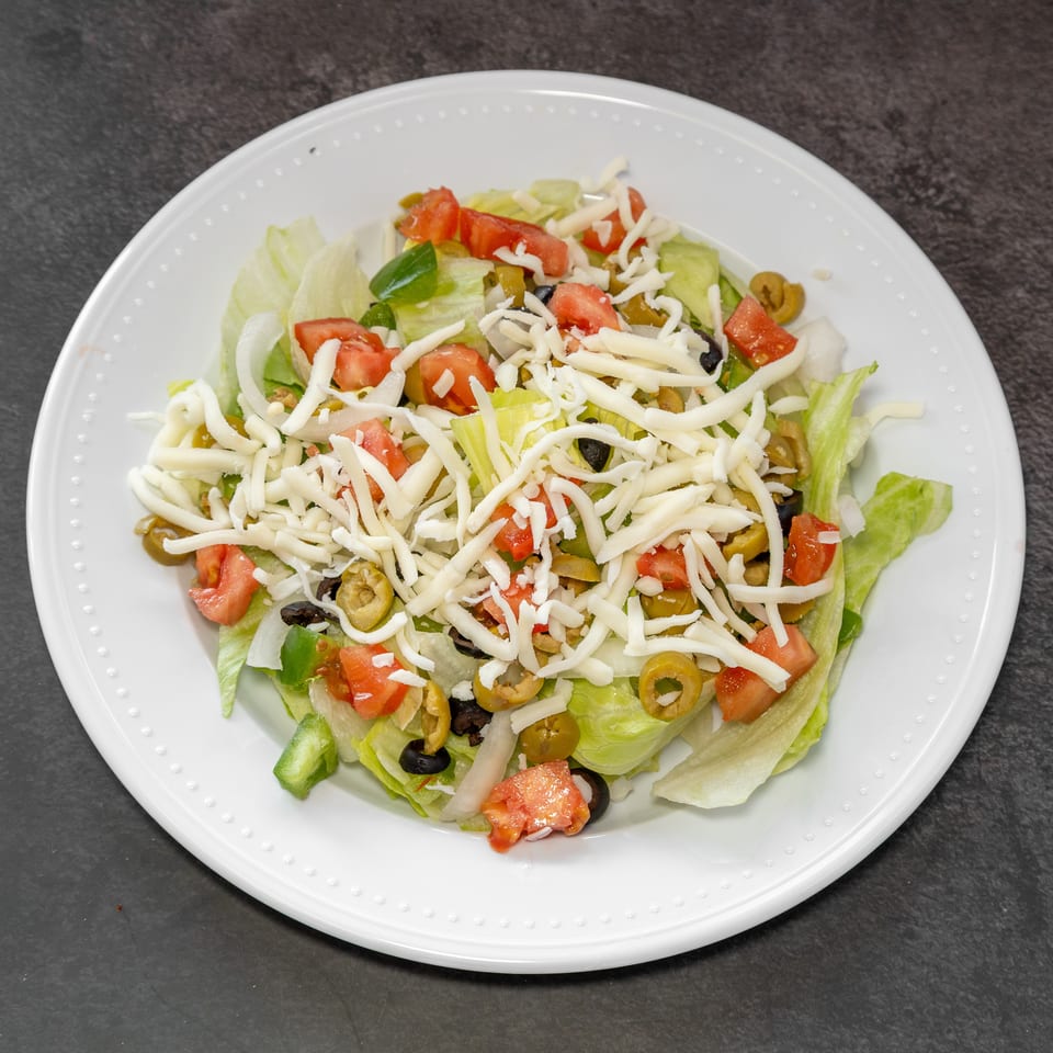 A fresh garden salad with lettuce, tomatoes, olives, onions, and shredded cheese on a white plate.